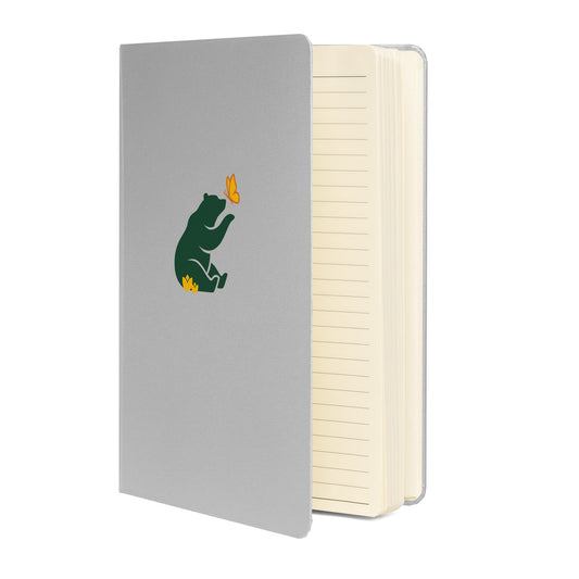 Gray (grey) notebook with green Petals & Paws bear graphic, sitting in yellow flowers with paw extended to yellow and orange butterfly. The book is standing up to reveal cream-colored, lined pages within.
