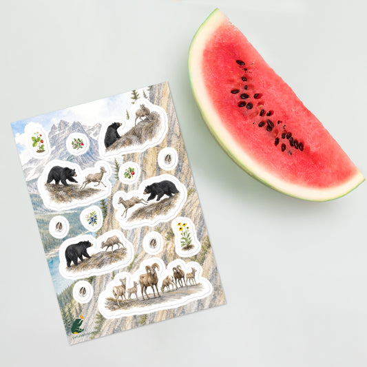 A sheet of kiss-cut stickers featuring black bear and bighorn sheep, botanicals, and roadway illustrations set against Rocky Mountain landscape, and placed next to a large slice of watermelon on a light gray background.