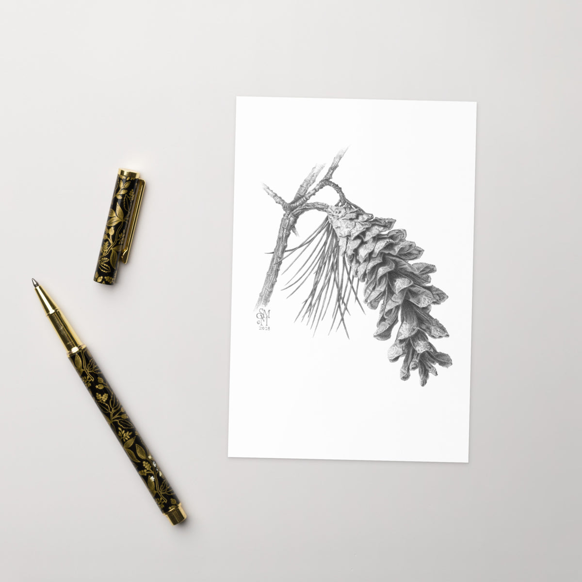Product mockup of the Pinus strobus - Eastern White Pine Greeting Card, shown with a fancy pen and cap on a beige surface.