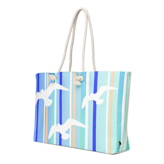 A diagonal view of Petals & Paws Tide Weekender Bag showing the pattern as it wraps around the ends of the bag, with the Petals & Paws logo near the bottom. This all-over print bag features seagull design with blue striped pattern and cream-colored cotton rope handles.