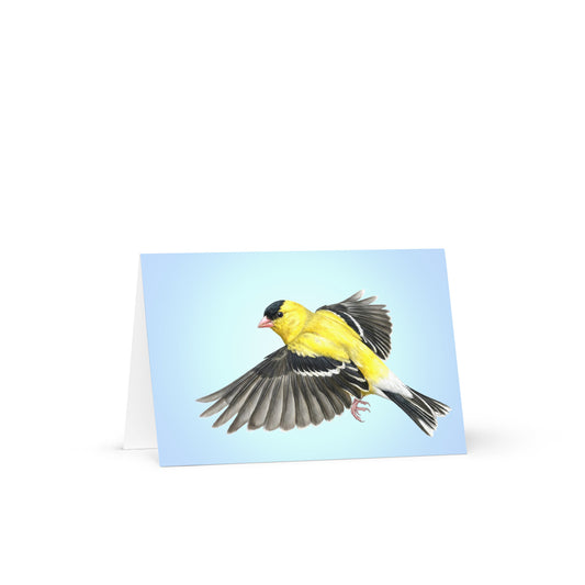 Product mockup of the American Goldfinch Greeting Card, standing open, with a realistic flying goldfinch against a clear blue sky.