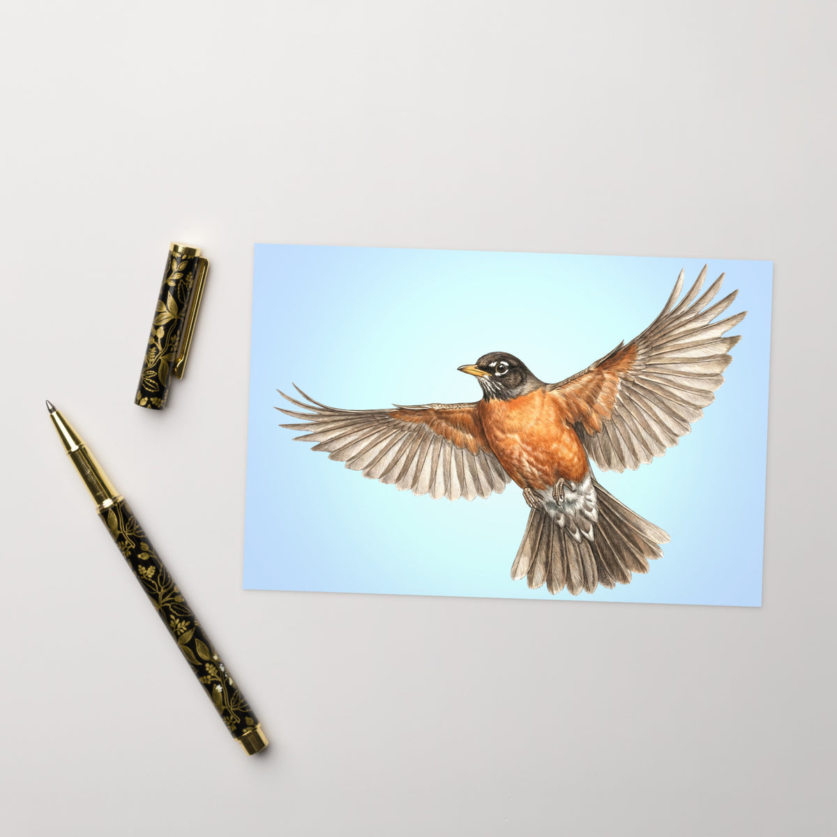 Product mockup of the American Robin Greeting Card, shown with a fancy pen and cap on a beige surface.