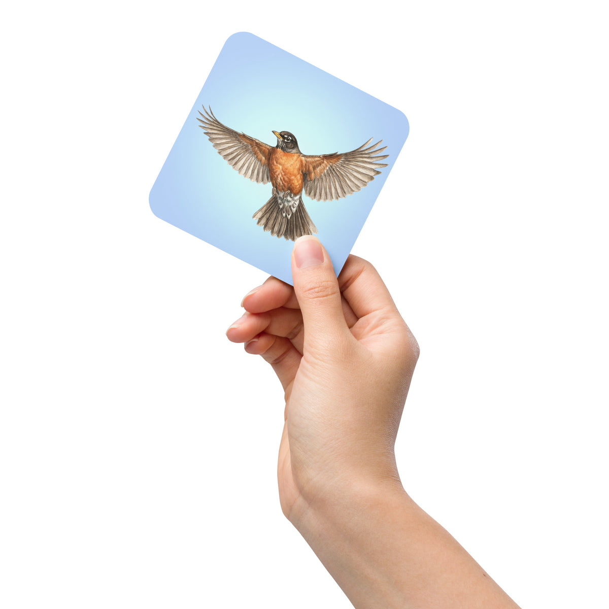 Product mockup of American Robin Coaster being held up by a woman's hand against a white background.  Robin is flying against a clear blue sky.