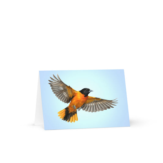 Product mockup of the Baltimore Oriole Greeting Card, standing open, with a realistic flying oriole against a clear blue sky.