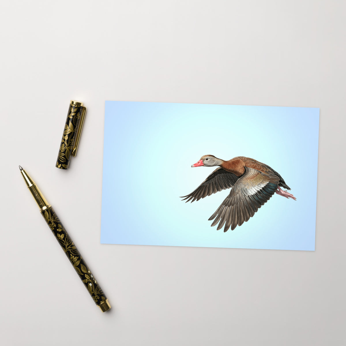 Product mockup of the Black-bellied Whistling Duck Greeting Card, shown with a fancy pen and cap on a beige surface.
