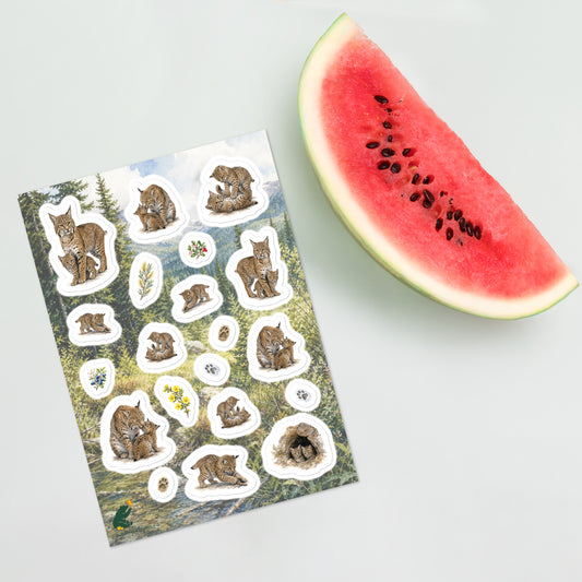 A sheet of kiss-cut stickers featuring illustrated bobcat mothers and kittens set against a scene in the foothills of the Rocky Mountains, and placed next to a slice of watermelon.  