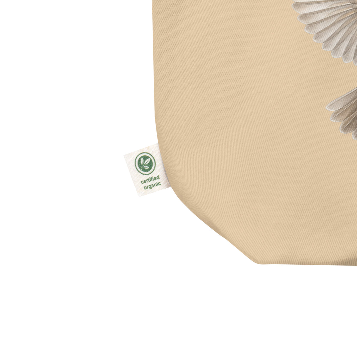 Product mockup showing a corner of the Cheerily Robin Eco Tote Bag with the certified organic tag extending out from it.  A portion of the ecru 100% organic cotton with robin wings and tail is visible.  