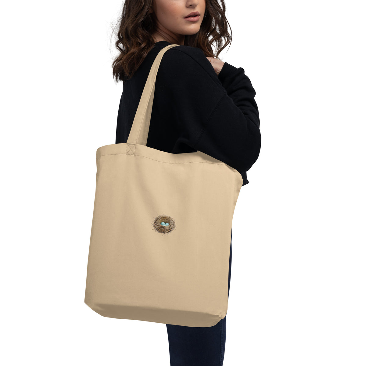 Product mockup of a woman carrying the Cheerily Robin with Nest Eco Tote Bag, revealing a beautiful robins nest with three robin-blue eggs inside, set against the ecru 100% organic cotton.  Two-side printed. 