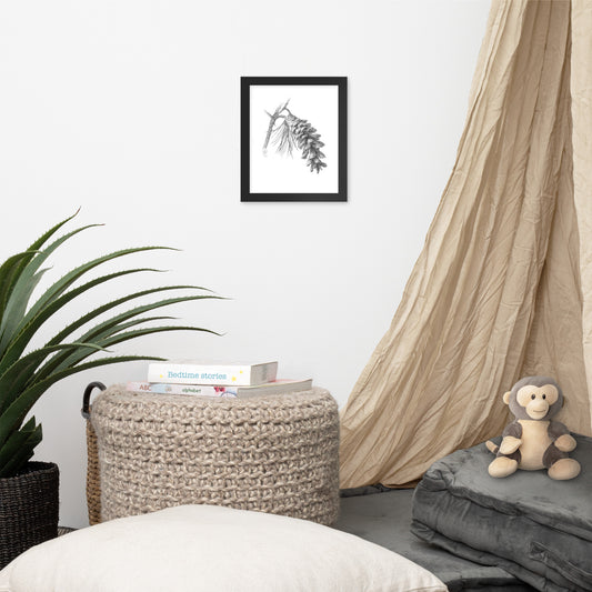 Black framed print of Pinus strobus - Eastern White Pine, graphite depiction of an Eastern white pinecone on a winter-bare branch, hanging on a wall with surrounding home furnishings.  Illustrated by Suzanne Matheson, 2017.