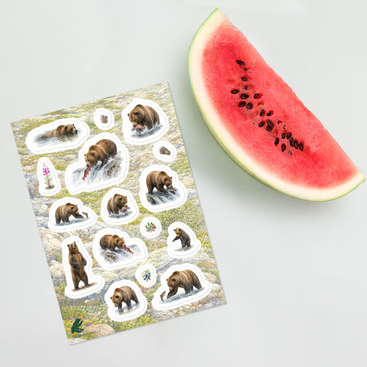 A sheet of kiss-cut stickers featuring illustrated grizzly bears fishing for salmon, with a background of rocky mountain icefields terrain, placed next to a slice of watermelon.