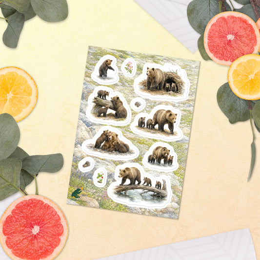 A sheet of kiss-cut stickers featuring illustrated grizzly bear families, with a background of rocky mountain icefields terrain, placed next to citrus slices on a warm-colored background.