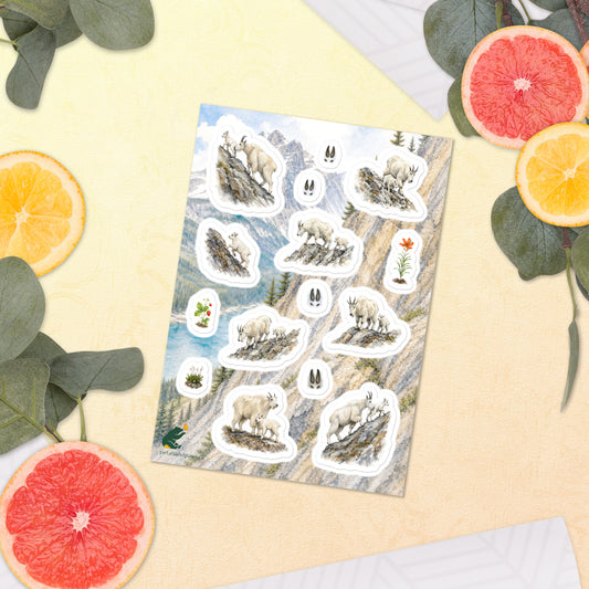 A sheet of kiss-cut stickers featuring Rocky Mountain landscape and mountain goat illustrations, placed next to citrus slices on a warm-colored background.
