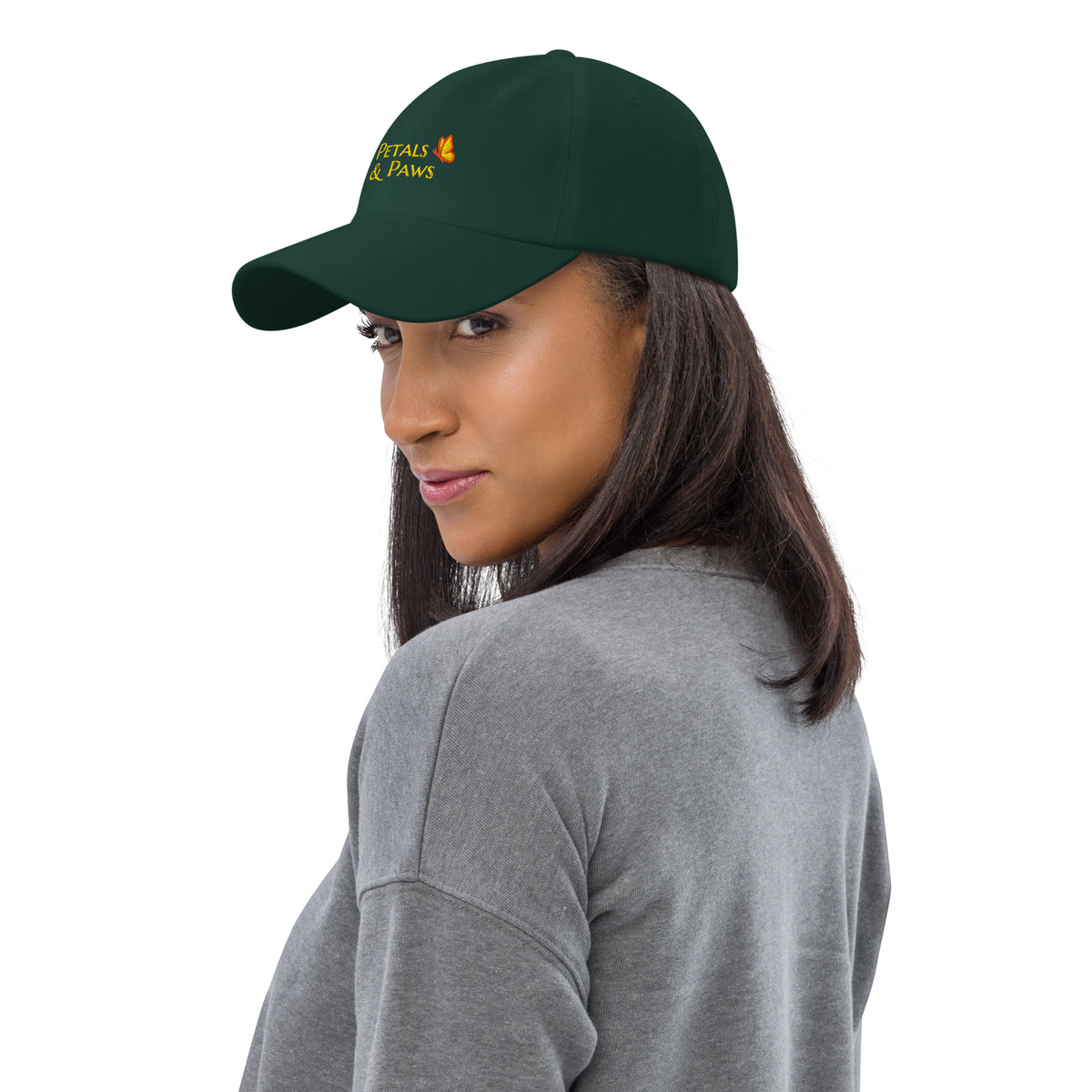A woman with brown hair wearing the spruce green Petals & Paws Classic Dad Hat, three-quarter view.