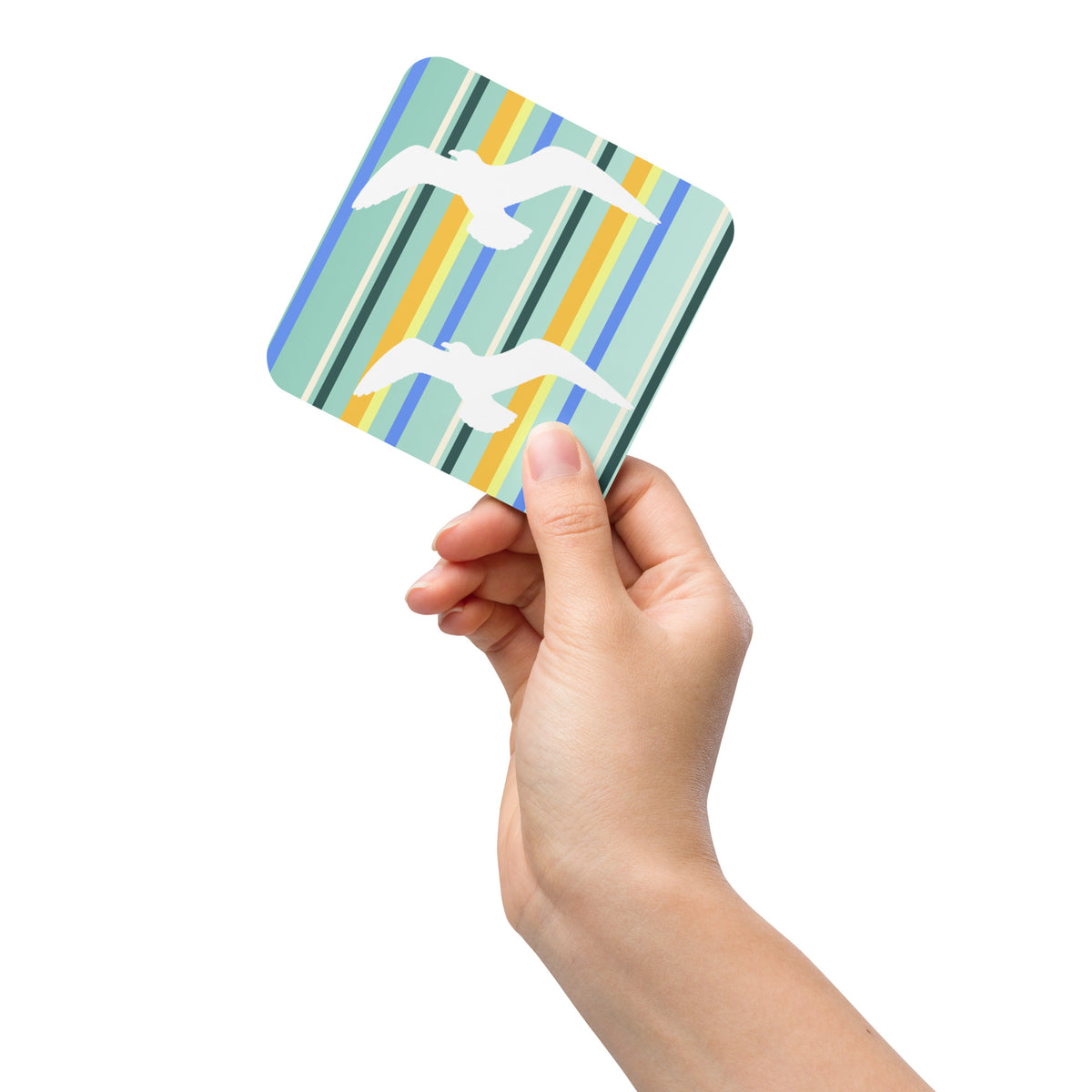 Product mockup of Petals & Paws Cove Coaster being held up by a woman's hand against a white background. Design is seagulls are flying against a teal striped pattern.
