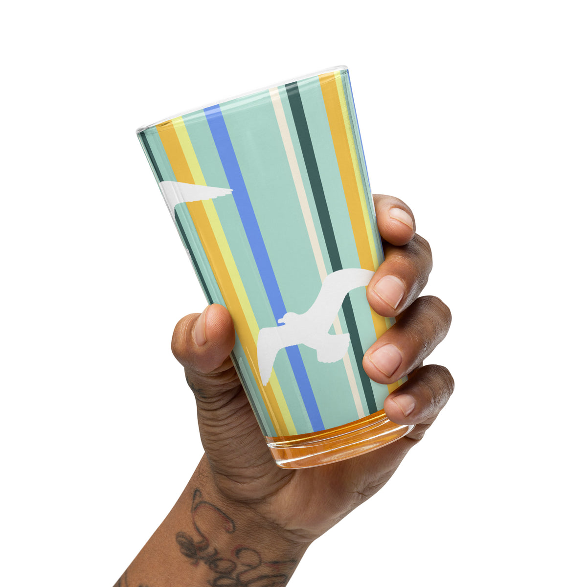 A hand extended from a tattooed arm tips the Petals & Paws Cove Pint Glass slightly.