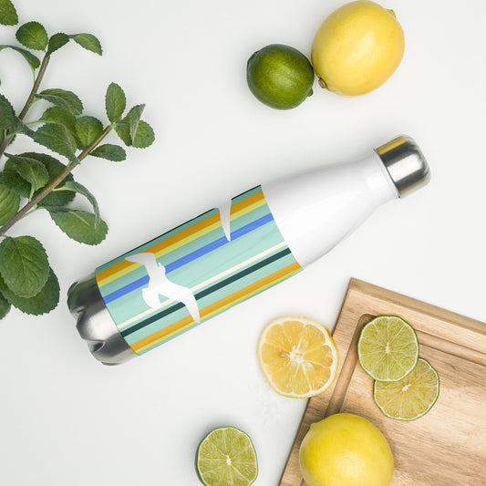 A 17 oz Petals & Paws Cove Water Bottle laying on its side amidst citrus fruit and an herb plant. This bottle features seagull design with teal striped pattern.