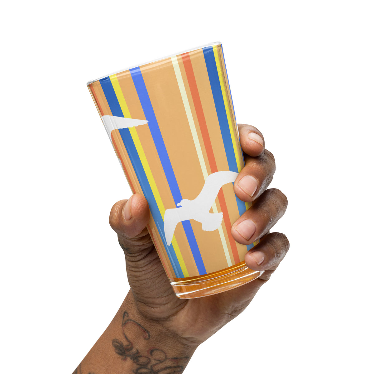 A hand extended from a tattooed arm tips the Petals & Paws Drift Pint Glass slightly.