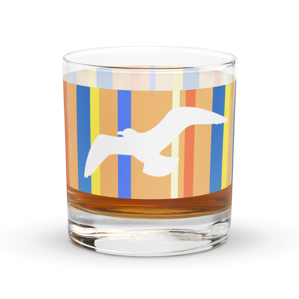 A Petals & Paws Drift Rocks Glass with a golden liquid inside it is sitting on a white surface. This glass features a seagull design with orange striped pattern.