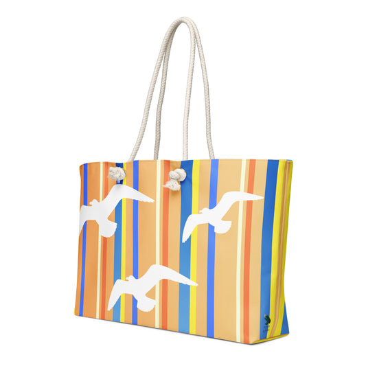 A diagonal view of Petals & Paws Drift Weekender Bag showing the pattern as it wraps around the ends of the bag, with the Petals & Paws logo near the bottom. This all-over print bag features seagull design with orange striped pattern and cream-colored cotton rope handles.