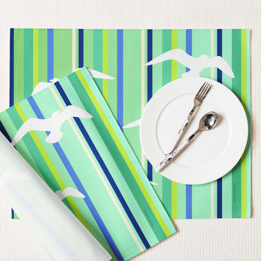 Product mockup of a Petals & Paws Harbour Placemat, featuring seagull design with green striped pattern. This image shows the white back and hemmed edges.