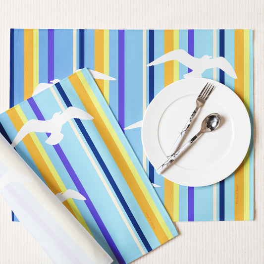 Product mockup of a Petals & Paws Shoreline Placemat, featuring seagull design with blue striped pattern. This image shows the white back and hemmed edges.