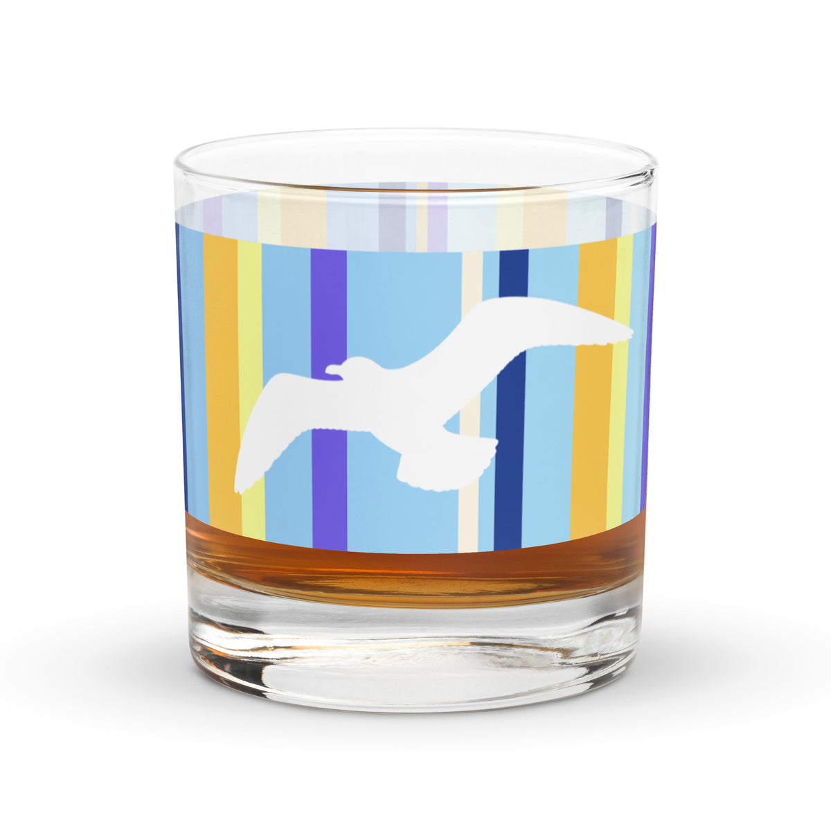 A Petals & Paws Shoreline Rocks Glass with a golden liquid inside it is sitting on a white surface. This glass features a seagull design with blue striped pattern.