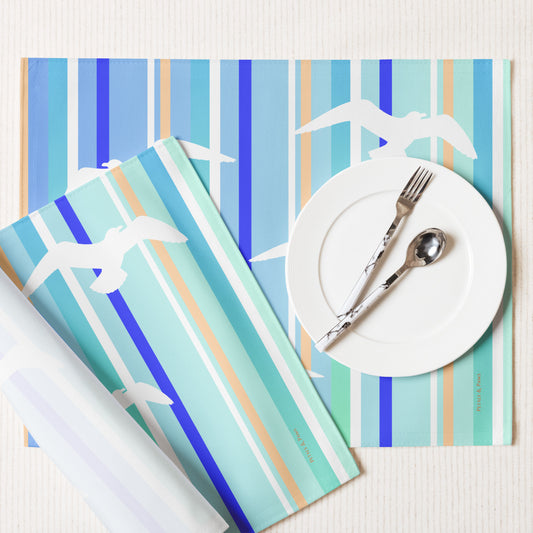 Product mockup of a Petals & Paws Tide Placemat, featuring seagull design with blue striped pattern. This image shows the white back and hemmed edges.