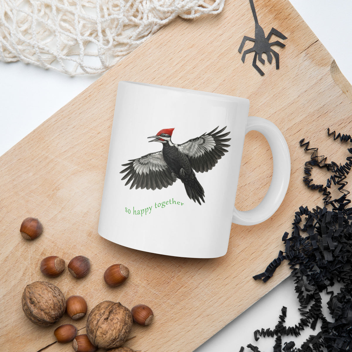Product mock-up of So Happy Together Pileated Woodpecker 11oz Mug laying on a cutting board with Halloween decorations surrounding.