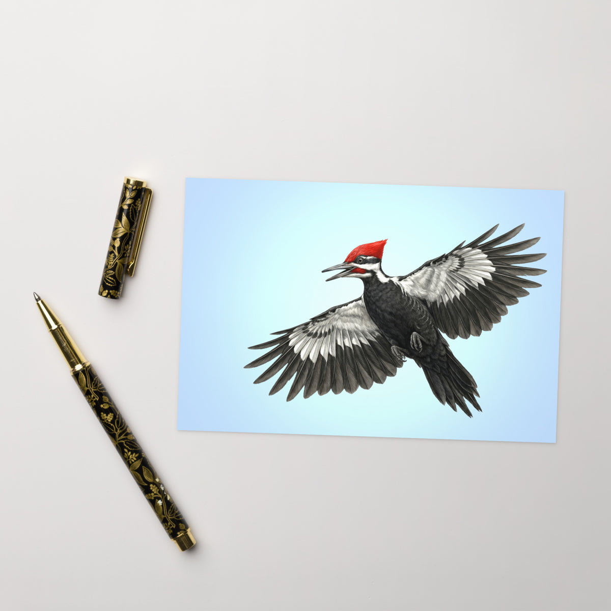 Product mockup of the Pileated Woodpecker Greeting Card, shown with a fancy pen and cap on a beige surface.