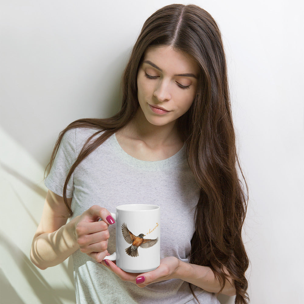 A woman holds and looks into 15 oz Robin Discovery Ceramic Mug.  Front design of realistic flying robin, "cheerio," set against a light T-shirt.