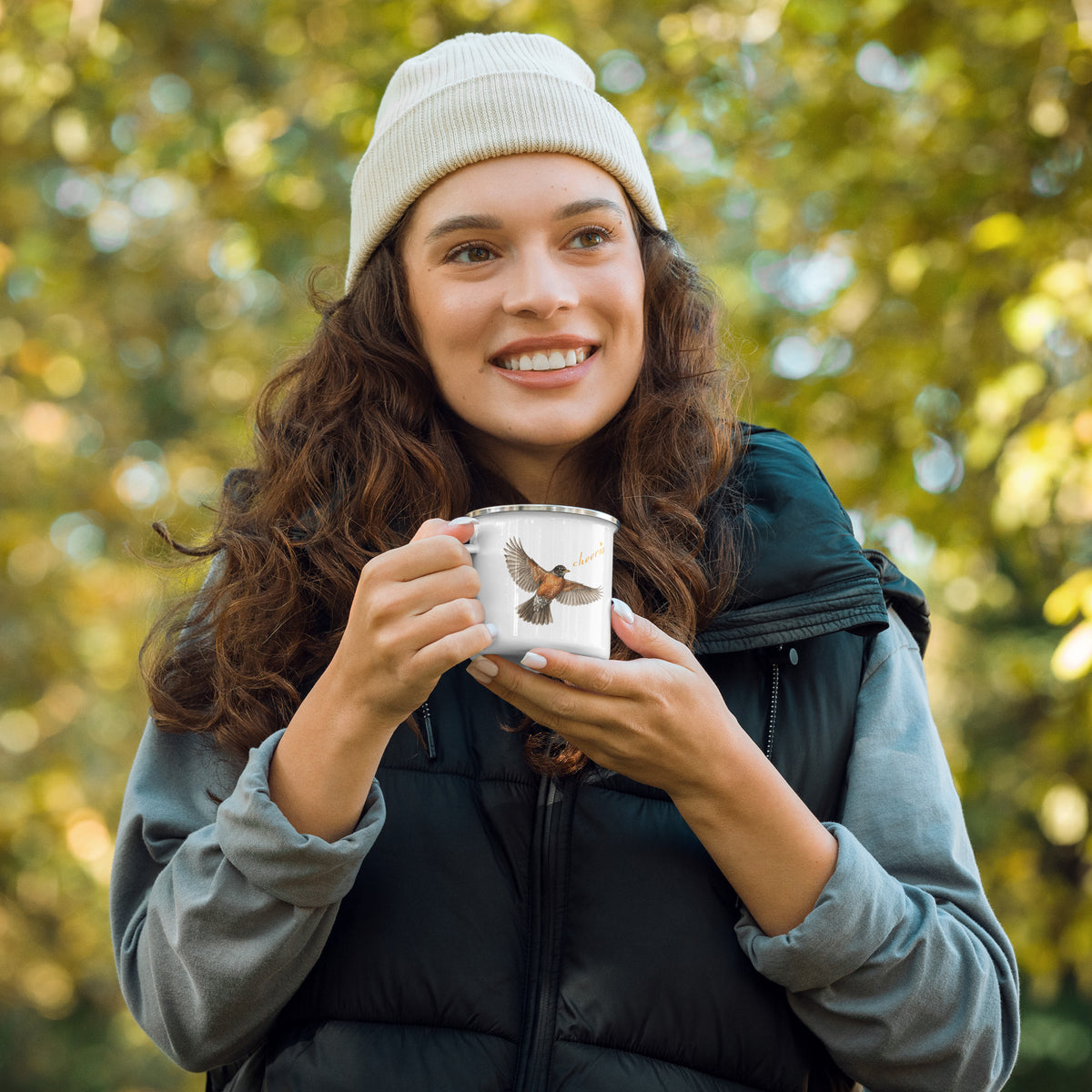 In-action shot of Robin Discovery Enamel Mug held in a woman's hands.  She is dressed for fall, with a blur of leaves behind her.