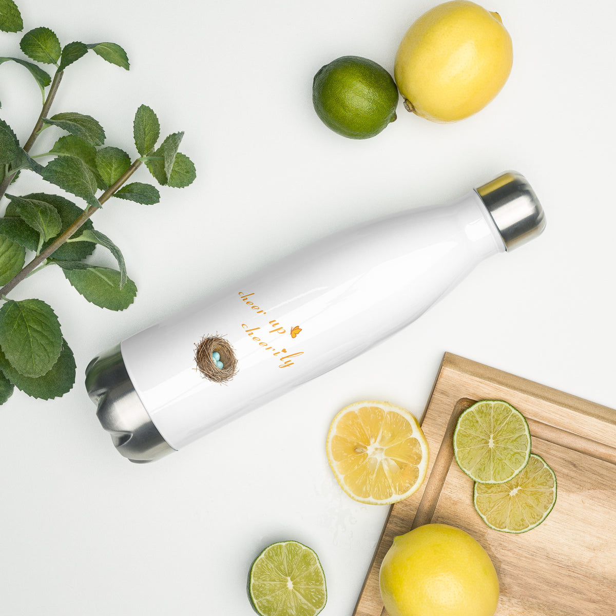 Product mockup of Robin Discovery Water Bottle laying on a white counter with a sprig of something green, lemons, limes, and a cutting board.
