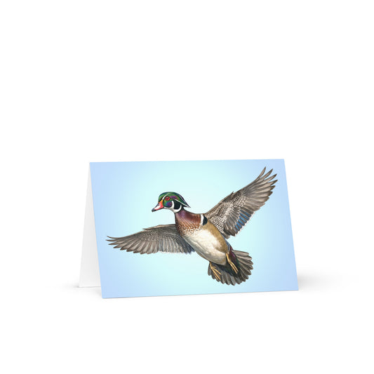 Product mockup of the Wood Duck Greeting Card, standing open, with a realistic flying duck against a clear blue sky.